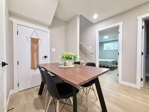 A dining area with a wooden table, black chairs, a macrame wall hanging, and a potted plant. - 2 BR Suite - Home Cinema - Location - Banff Pass (Calgary)