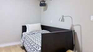 Un lit simple avec une couvre-lit à motifs, une lampe de chevet et un projecteur fixé au plafond.
