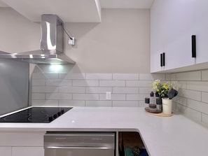 Uma cozinha moderna com fogão embutido, coifa de aço inoxidável e azulejos brancos tipo metrô na parede de proteção.