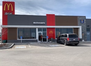 A McDonald's restaurant with a parking lot and a visible entrance. - 2 BR Suite - Home Cinema - Location - Banff Pass (Calgary)