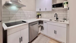 Une cuisine moderne avec des meubles blancs, une hotte en acier inoxydable, une plaque de cuisson à induction noire, un lave-vaisselle et un four à micro-ondes.