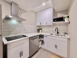 Cozinha moderna com armários brancos, exaustor de aço inoxidável, fogão por indução preto, lava-louças e micro-ondas.