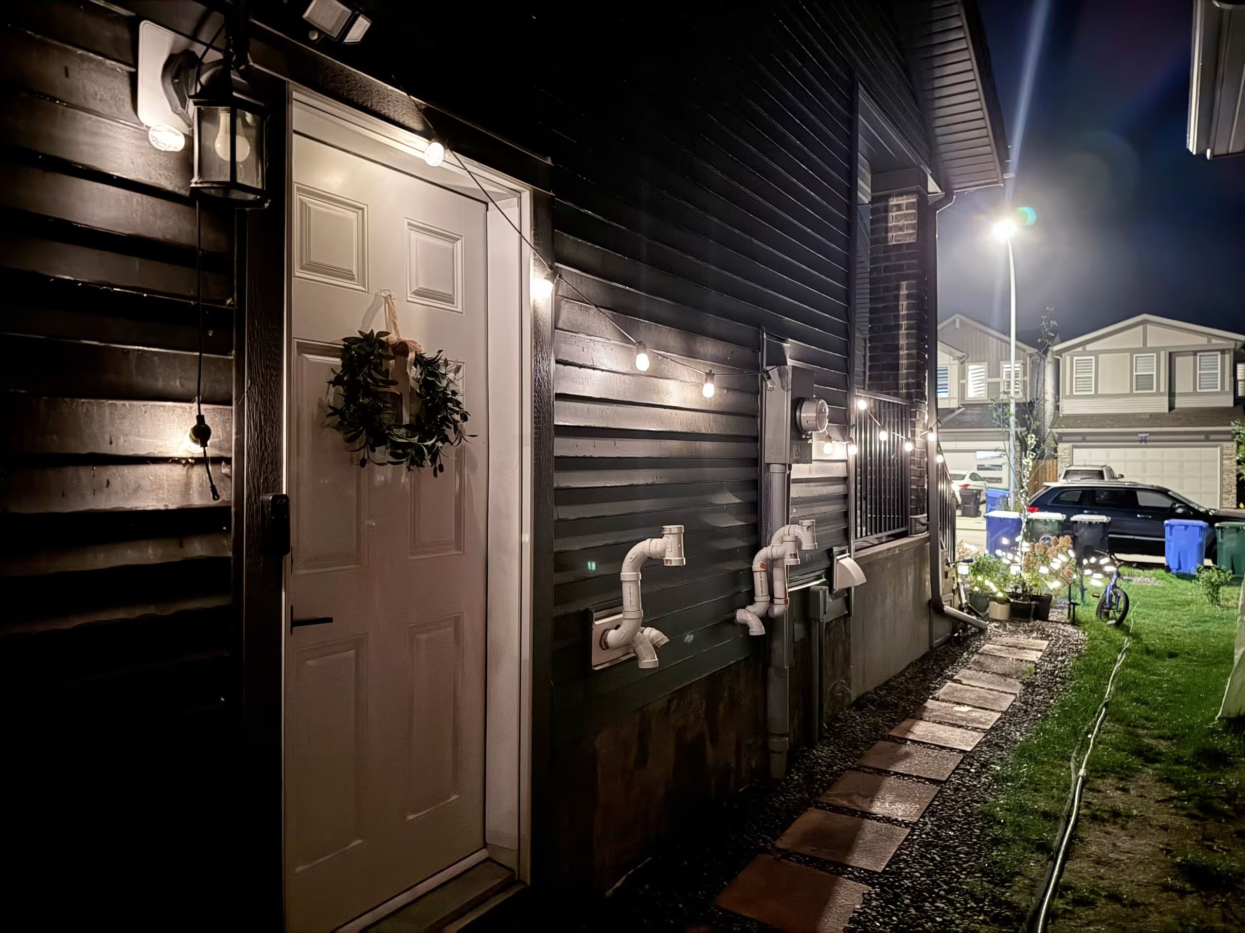 Une maison avec une porte blanche, une guirlande décorative, un éclairage extérieur et un chemin menant au garage.