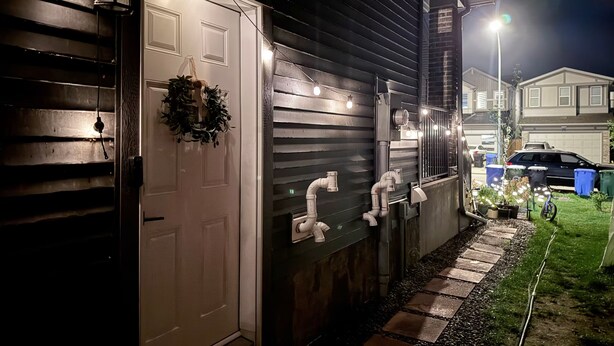 Une maison avec une porte blanche, une guirlande décorative, un éclairage extérieur et un chemin menant au garage.
