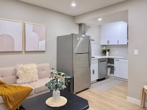 Cozinha moderna com armários brancos, geladeira de aço inoxidável e área de jantar com mesa preta e sofá com manta amarela.