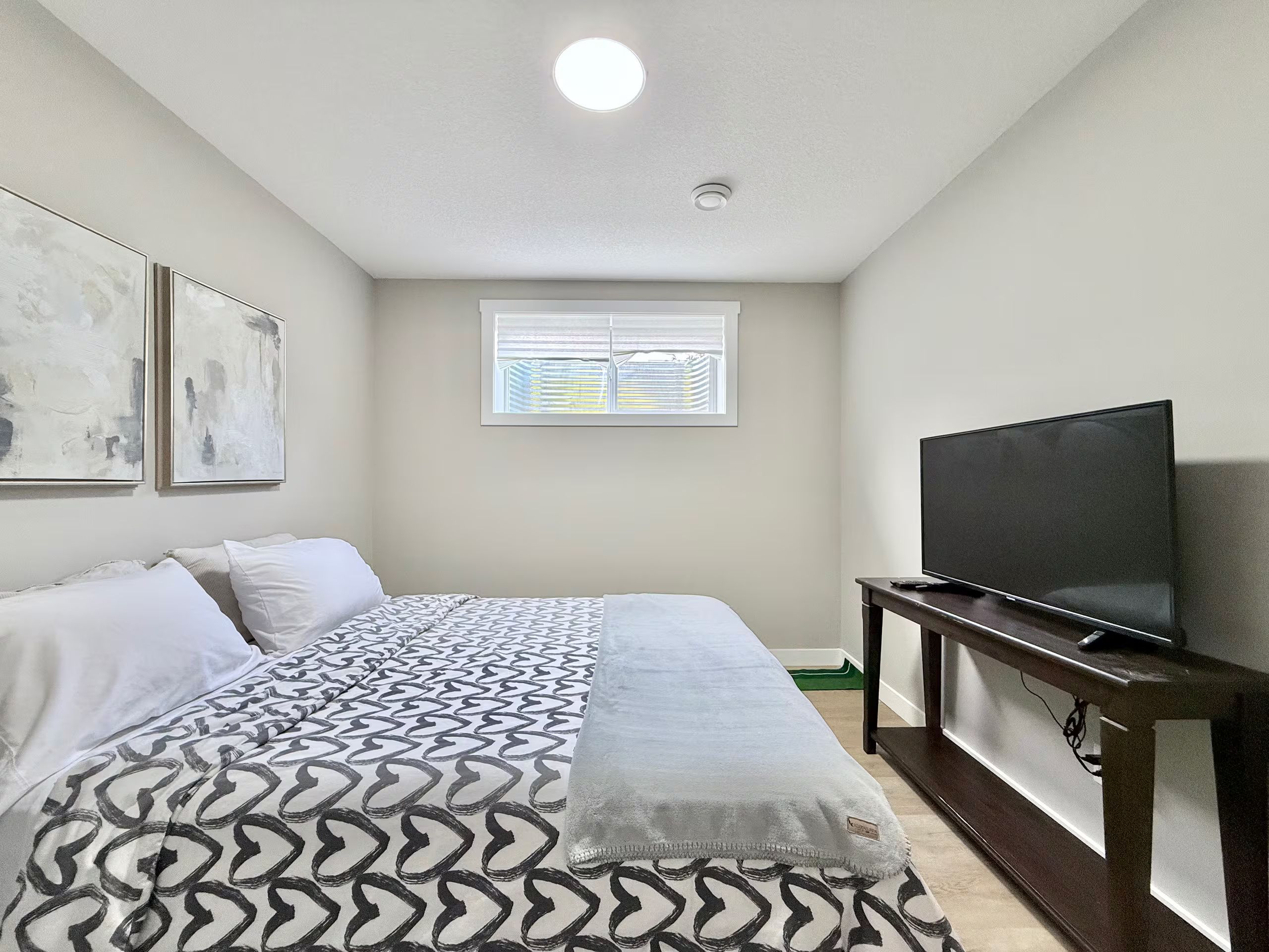 Une chambre à coucher avec un lit, un téléviseur posé sur un meuble et une fenêtre avec des stores.