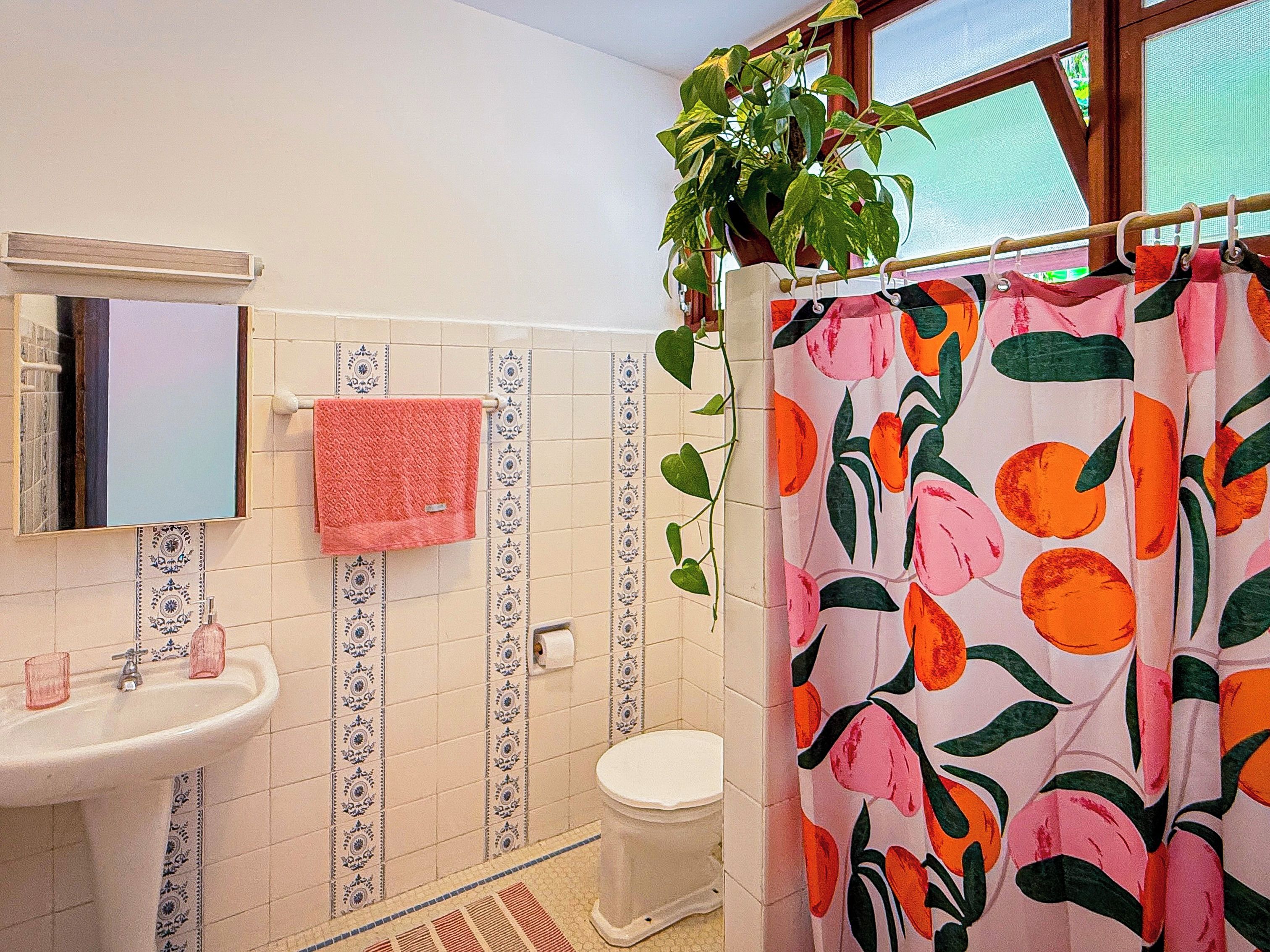 A bathroom with a sink, toilet, and shower curtain with a fruit pattern.