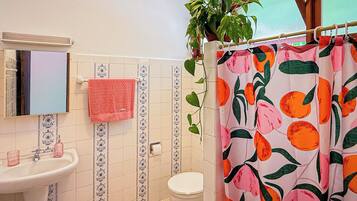 A bathroom with a sink, toilet, and shower curtain with a fruit pattern.