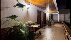 An outdoor patio area with a table and chairs, potted plants, and a wall-mounted light fixture.