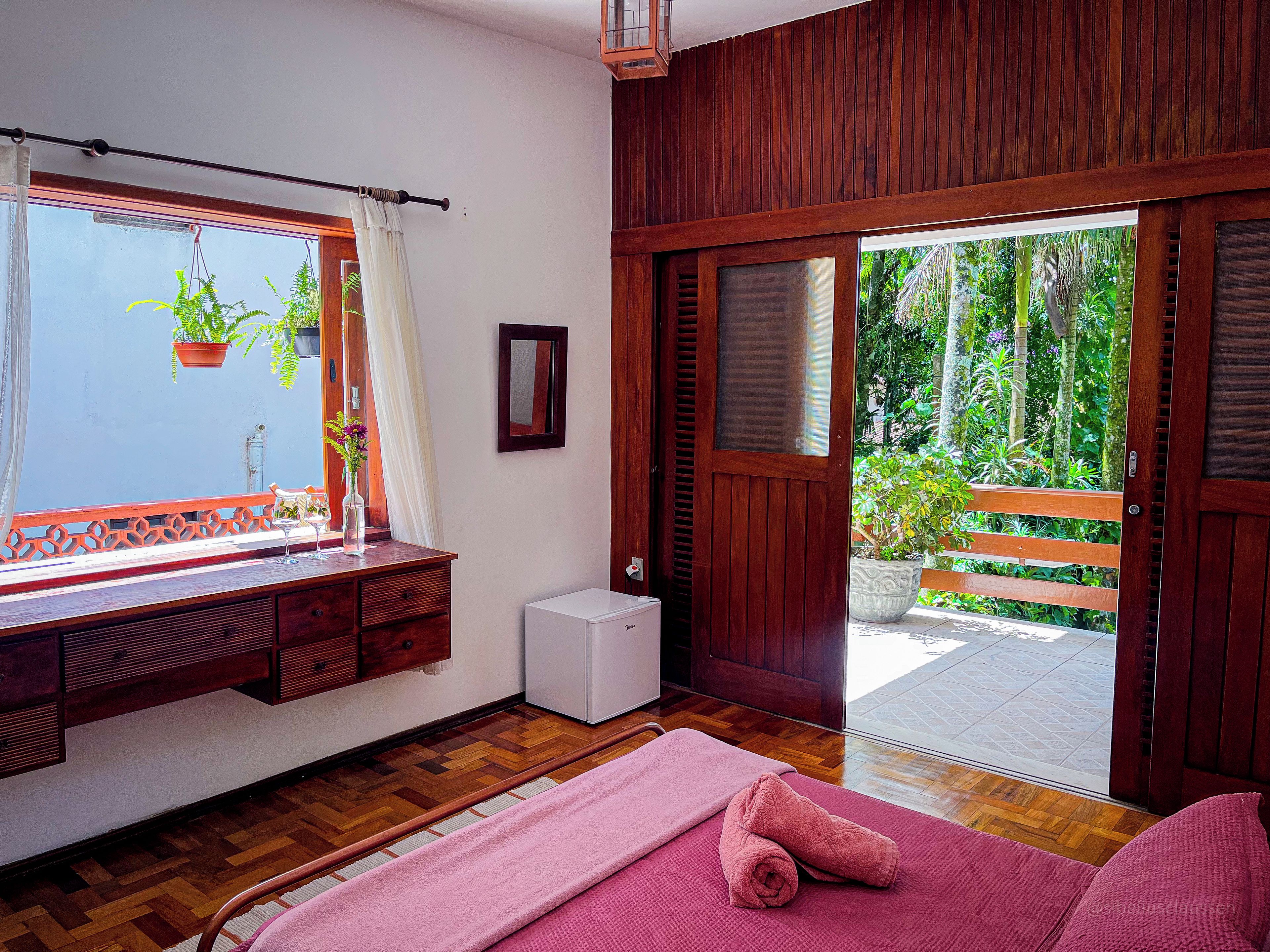 A room with a wooden bench, a small white appliance, a pink towel, and a view of greenery outside.