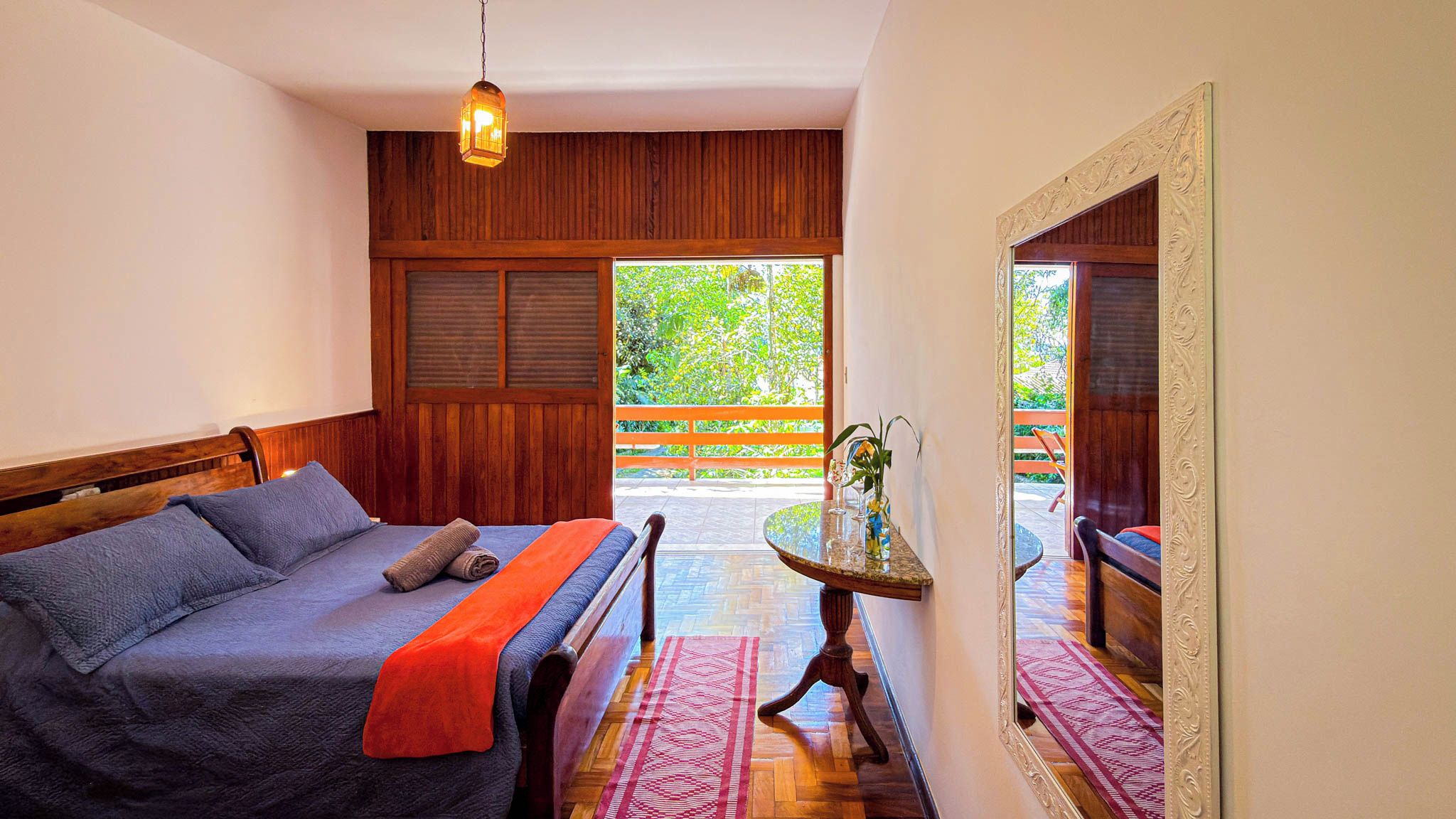 A bedroom with a bed, a nightstand, a mirror, and a view of the outdoors.