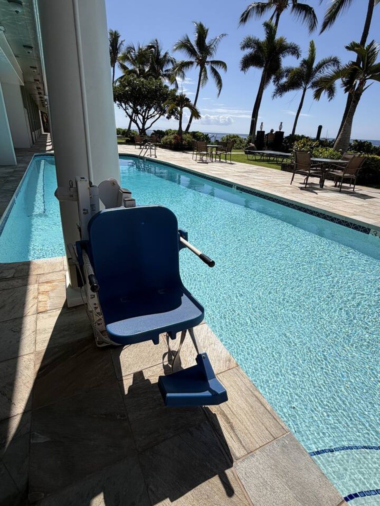 A poolside area with a blue chair, palm trees, and a clear view of the ocean.