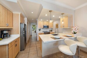 A modern kitchen with wooden cabinets, a central island, bar stools, and a coffee maker. - Lahaina Shores Beach Resort, Ocean Views Sleeps 5 (Lahaina)