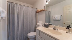 A bathroom with a striped shower curtain, a toilet, a sink with a mirror, and a towel rack. - Lake Mode: ON - 2 Bedroom Waterfront Condo (Lake Ozark)