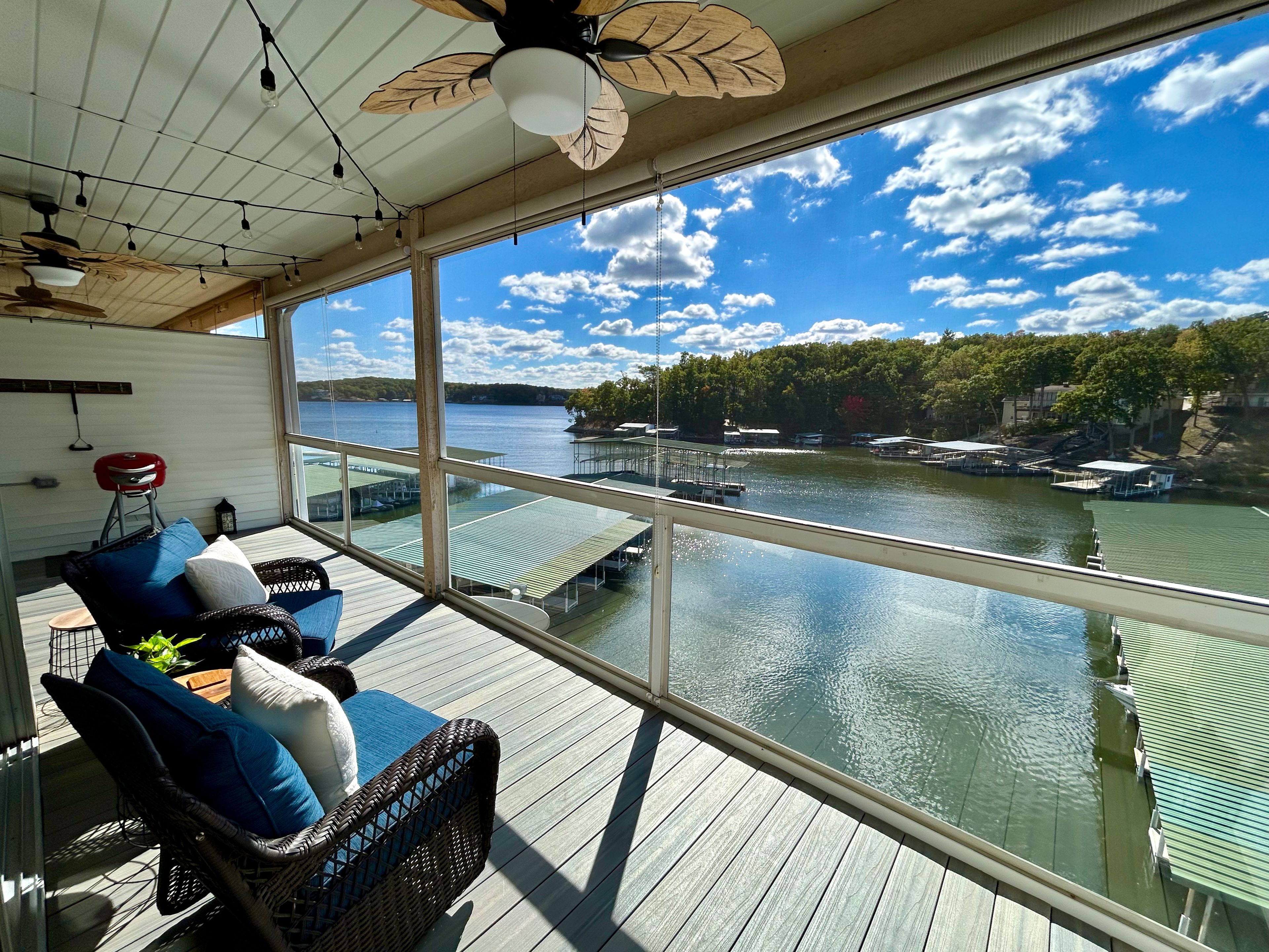 A spacious balcony with a view of a lake, furnished with wicker chairs and a red bar stool.
