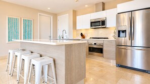 A modern kitchen with a central island, stainless steel appliances, and a bar stool seating arrangement. - Serene Retreat 2BR in Plaza Puntarena (Río Hato)