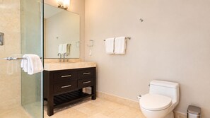 A modern bathroom with a glass shower enclosure, a dark vanity with multiple drawers, a white toilet, and a mirror with lights. - Serene Retreat 2BR in Plaza Puntarena (Río Hato)