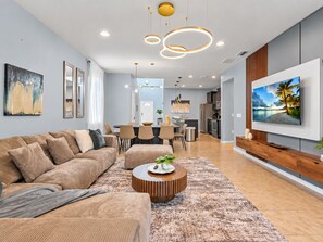 A modern living room with a sectional sofa, a coffee table, and a TV mounted on the wall. - 6BR Disney Area Home | Pool, Spa & Resort (Kissimmee)