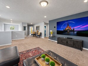 Ein modernes Wohnzimmer mit einem Flachbildfernseher, einem Ledersofa, einem Couchtisch mit dekorativen Pflanzen und einem gemusterten Teppich.