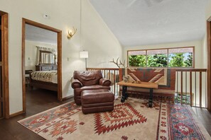 A spacious room with a large window, a brown leather chair, a patterned rug, and a wooden bench. - Angel Fire Haus (Angel Fire)