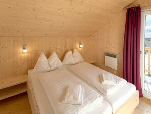 Ein Zimmer einer Holzhütte mit zwei Betten, einem Fenster mit Vorhang und einem fest montierten Heizkörper.