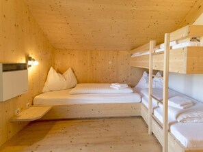 Habitació d'una cabana de fusta amb llits superposats, un escalfador penjat a la paret i una petita estant.