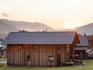 Una cabana de fusta amb teulat inclinat, un porxo amb seients i vista als voltants de les muntanyes.