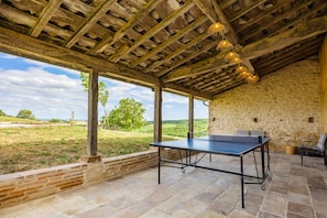 A covered outdoor area with a ping pong table, stone walls, and a view of the countryside.