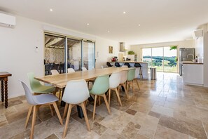 Een moderne keuken met een groot eiland, een eethoek met een houten tafel en kleurrijke stoelen, en uitzicht op het platteland door grote ramen.