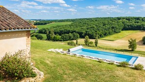 Una piscina con vistas a un paisaje verde y un edificio con techo de tejas.
