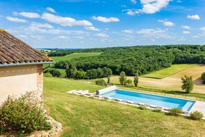 Ein Pool mit Blick auf eine grüne Landschaft und ein Gebäude mit einem Ziegeldach.