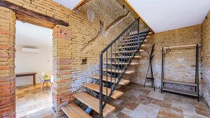 Un interior rústico con paredes de ladrillo visto, una escalera de madera y un suelo de baldosas.