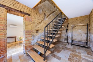 Ein rustikales Interieur mit freiliegenden Backsteinwänden, einer Holztreppe und einem Fliesenboden.