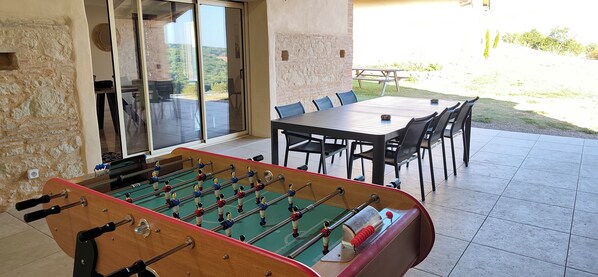 A foosball table in a room with a patio area, a table and chairs, and a view of the outdoors.