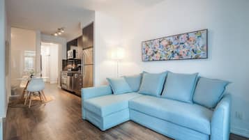 A modern living room with a light blue sectional sofa, a dining area with a white table and chairs, and a kitchen in the background.