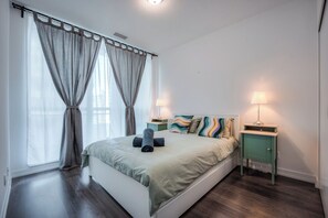 A bedroom with a bed, curtains, a bedside table with a lamp, and a wall-mounted shelf. - Modern 2BR Condo in Midtown Toronto with Balcony (Toronto)
