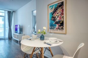 A dining area with a round table, white chairs, a vase with flowers, and a framed picture on the wall.