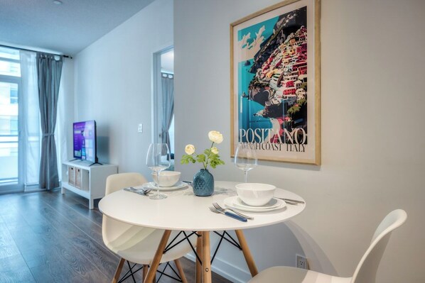 A dining area with a round table, white chairs, a vase with flowers, and a framed picture on the wall.