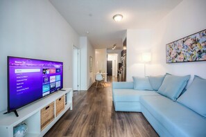 A modern living room with a flat-screen TV displaying a Roku interface, a light blue sofa, and a wooden floor.