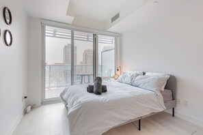 Ein modernes Schlafzimmer mit einem großen Bett, einer Schiebetür zum Balkon und Blick auf die Stadt.