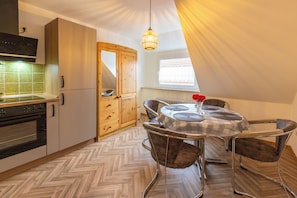 A compact kitchen with modern appliances, a dining area with a checkered tablecloth, and a view of the outside through a window. - Behind Mill B (Krummhörn)