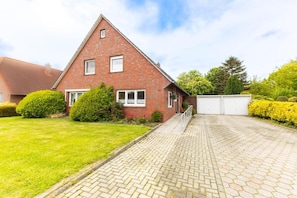 A red brick house with a paved driveway and a white garage door. - Behind Mill B (Krummhörn)