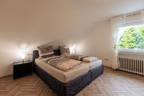 A bedroom with a bed, nightstands, a window with curtains, and a radiator. - Behind Mill B (Krummhörn)