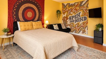 A bedroom with a large bed, a tapestry, a motivational poster, a TV, and a small side table.