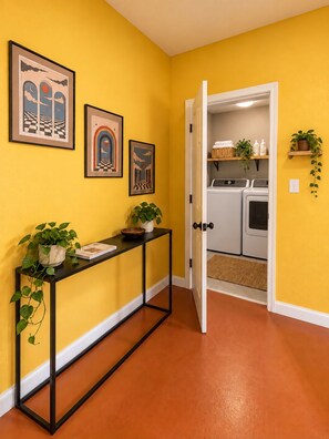 A hallway with a yellow wall, a black console table with a plant, and framed artwork.