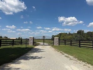 A gravel path leading to a gated entrance with stone pillars and a metal gate.