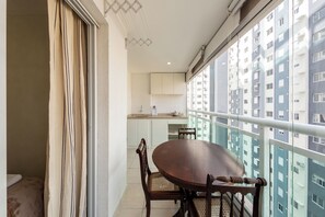 A balcony with a dining table and chairs, a kitchen area in the background, and a view of a residential building. - Almeida by Bhomy  (São Paulo)