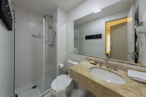 A modern bathroom with a glass shower enclosure, a toilet, a sink with a mirror, and a towel rack. - Almeida by Bhomy  (São Paulo)