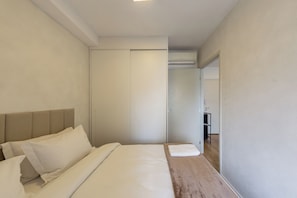 Ett hotellrum med en säng, ett träbord vid sängen, en garderob och en dörr som leder till ett badrum.