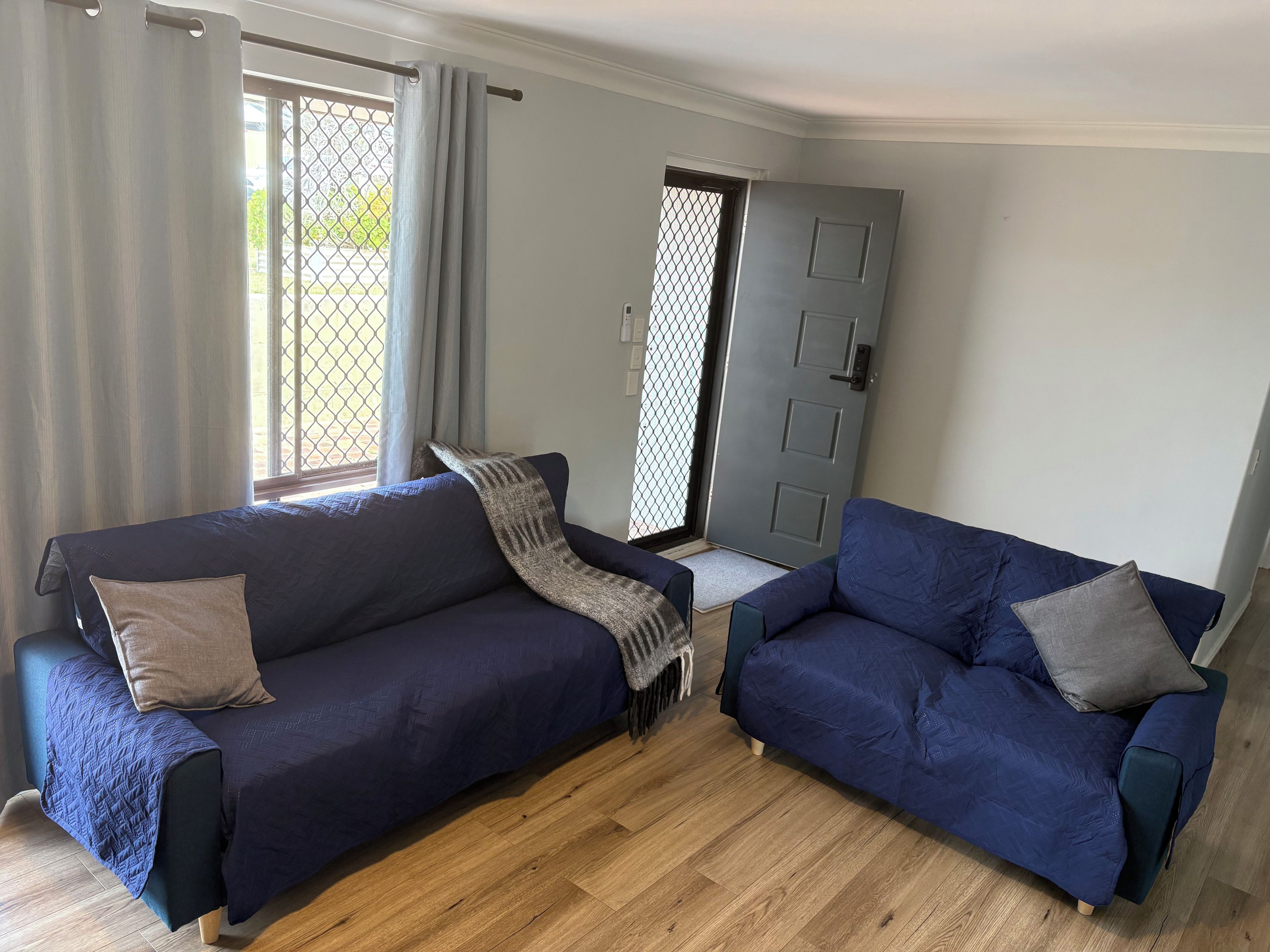 A room with two dark blue sofas, a grey door, and a window with curtains.